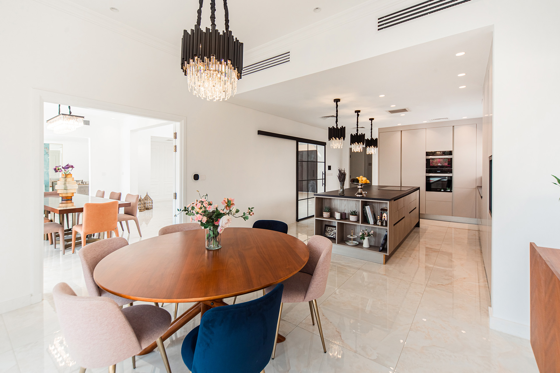 Open plan layout of dining room and kitchen, designed by Smart Renovation for Villa Chanel, featuring statement ceiling lights