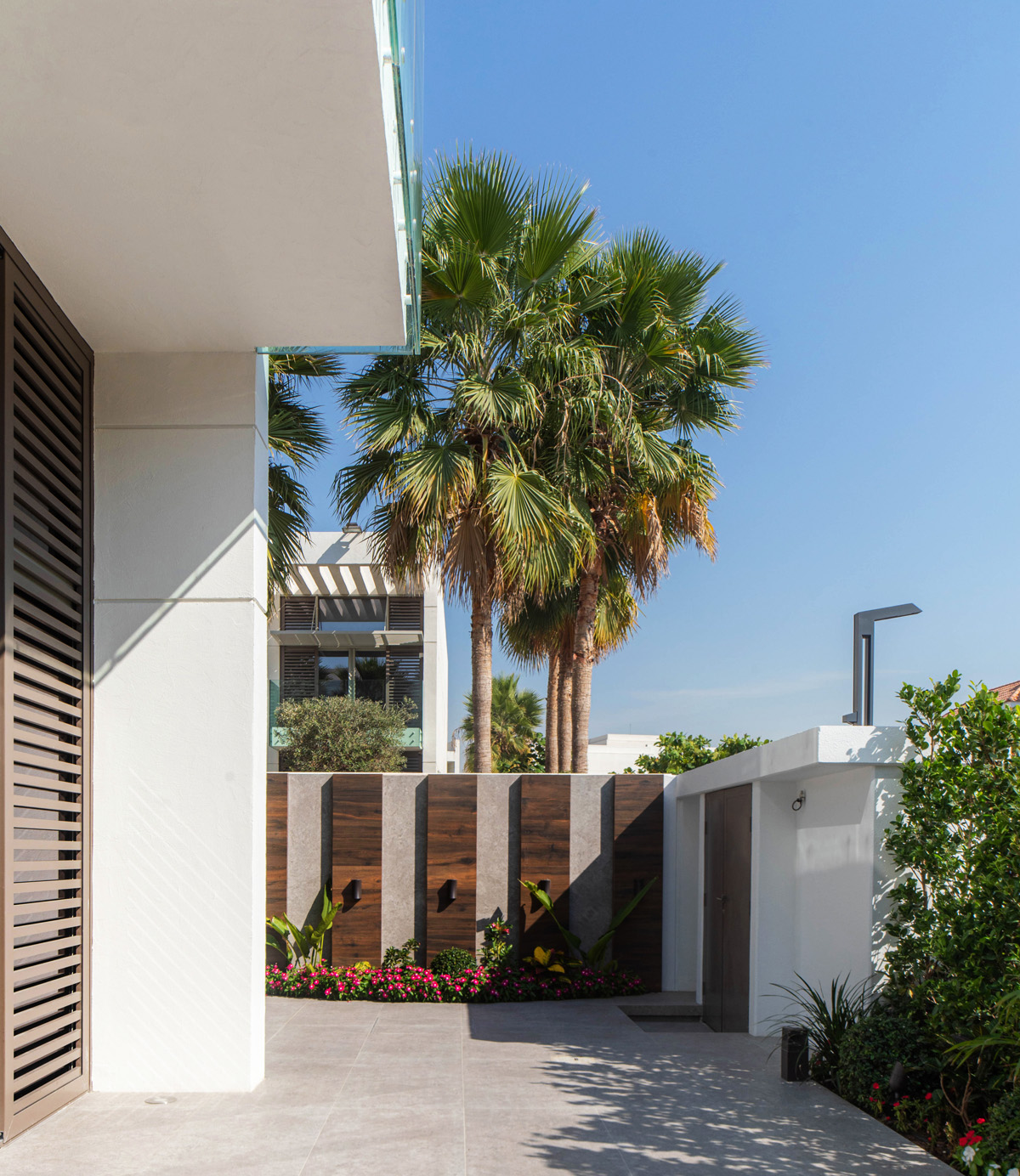 Garden landscaping Dubai with minimal stone tiles, palm trees, and vertical wood paneling for luxury villas.