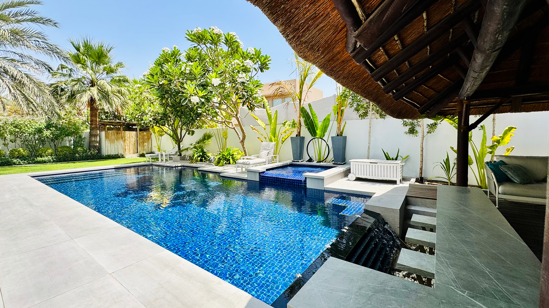 Tropical garden pool by Smart Renovation for Casa Porto Cervo with lush greenery, blue tiles, spa, and shaded seating area.
