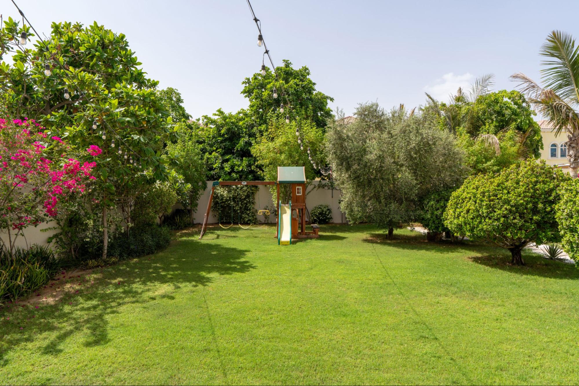 Open lawn concept by Smart Renovation for Casa Fiorita featuring mature trees, flowering plants, and a child-friendly play zone.