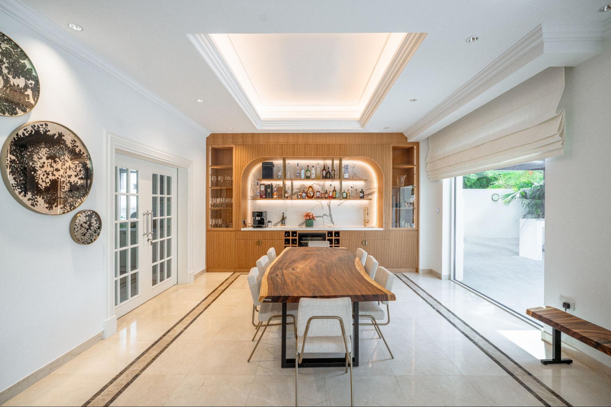 Contemporary dining and bar area design by Smart Renovation for Villa Camellia featuring a live-edge wood table and built-in cabinetry.